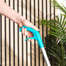 Close-up of hand holding a blue grabber tool with trigger, against wooden slats and plants.