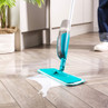 Blue spray mop cleaning a liquid spill on wood floor