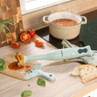 Green hand blender on kitchen counter with tomato soup and sliced bread