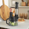 Electric food processor with handle and stainless steel detail, slicing cucumber, on kitchen counter