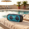 Portable blue wireless speaker by swimming pool, shown on beige towel