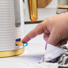 White and gold electric kettle being switched on by hand, close-up of power button.