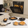 Set of black non-stick bakeware with baked goods on kitchen worktop and in oven