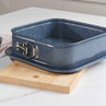 Square blue speckled springform cake tin with latch, shown empty on kitchen worktop