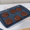 Six chocolate cookies on a baking tray, shown fresh from the oven.