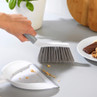 Grey and white handheld brush and dustpan set sweeping crumbs from a kitchen worktop