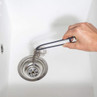 Hand using black tongs to remove hair from a kitchen sink drain