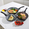 Set of three black non-stick frying pans with cooked fish, chicken, and vegetables.