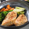 Two cooked chicken breasts with carrots, broccoli, and leeks in a non-stick frying pan