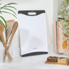 White plastic chopping board with black edges, shown upright on kitchen counter