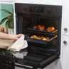 Hand using tea towel to remove baked croissants and roast potatoes from modern oven