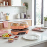 Orange electric burger maker with buns and patties in a modern kitchen setting