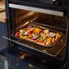 Oven tray with assorted chopped vegetables roasting, showing peppers, carrots, onion and potatoes.