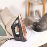 Cordless black and copper steam iron on ironing board with steam, in a home setting