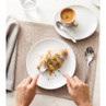 Person cutting pistachio croissant on white plate with coffee, for breakfast tableware listing