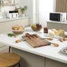 Cheese board set with wooden knives on marble kitchen countertop, bread and grapes displayed