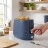 2-slice blue toaster with toast, hand pressing lever, on kitchen counter