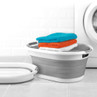 Grey collapsible laundry basket shown open and folded, in front of washing machine.