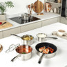 Set of stainless steel saucepans and frying pan with food, shown in a modern kitchen