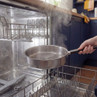Steam rises from clean silver frying pan after dishwasher cycle