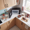 Black microwave with open door on kitchen counter, baking ingredients and utensils nearby