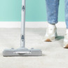 Upright vacuum cleaner head cleaning cream carpet, person in jeans and trainers visible.
