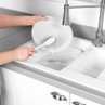 Washing up brush cleaning a white plate in kitchen sink with running tap