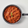 Pan of beef Bolognese sauce garnished with basil, shown from above.