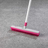 Pink and white rubber broom on grey carpet, shown cleaning pile.
