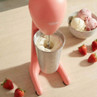 Pink milkshake maker with stainless steel cup, shown mixing milkshake next to strawberries and ice cream.