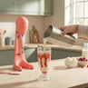 Strawberry milkshake being poured into a tall glass with a pink drink mixer in the background