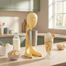 Yellow milkshake maker with metal jug on kitchen counter, ingredients and banana shake beside