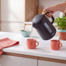 Modern black electric kettle pouring water into coral mugs on kitchen counter