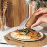 Hand using wooden salt or pepper grinder over cooked chicken, salad and couscous on table