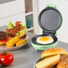 Green mini electric grill with fried egg, shown beside burger and buns on kitchen counter