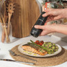 Black electric salt or pepper grinder seasoning salmon fillet and vegetables on plate