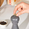 Hand adjusting black pepper mill, bowl of peppercorns in background