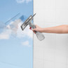 Hand holding grey window vacuum cleaner on white tiled wall