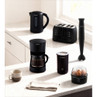 Glass coffee carafe with black handle pouring coffee into mug on kitchen counter