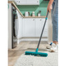 Person using blue rubber broom to clean rug in a modern white kitchen