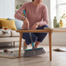 Woman sweeping under wooden coffee table with grey and blue broom in modern living room