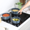 Set of blue non-stick saucepans with food on an induction hob, hand holding handle