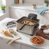 Stainless steel deep fat fryer with fresh churros in kitchen setting, prep items beside