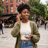 Blue wireless earbuds and charging case held outdoors, street view, casual wear