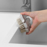 Grey cleaning brush with white bristles held over a kitchen sink