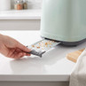 Hand removing crumb tray from green toaster to show easy cleaning feature