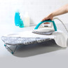 Teal and white electric iron being used on a shirt, shown on a patterned ironing board.