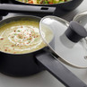 Grey non-stick saucepan with glass lid, shown with creamy soup, for product listing.