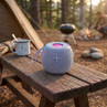 Portable blue wireless speaker with handle on outdoor wooden bench at campsite