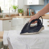 Navy steam iron pressing white shirt in modern kitchen, showing anti-drip feature.